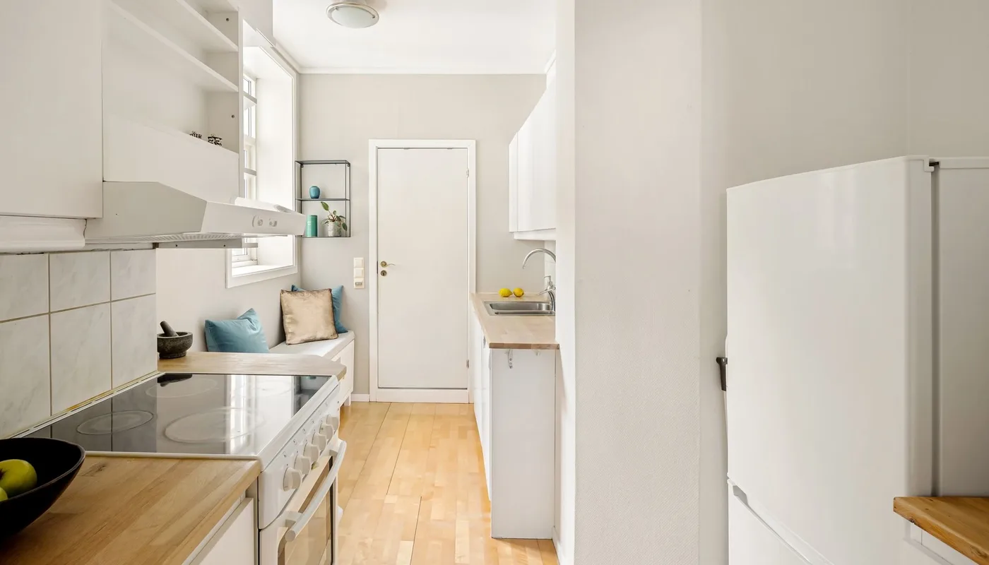 A clean galley kitchen with white units, wooden worktops and a ceramic hob, the kind of room a check-in report has to record in detail