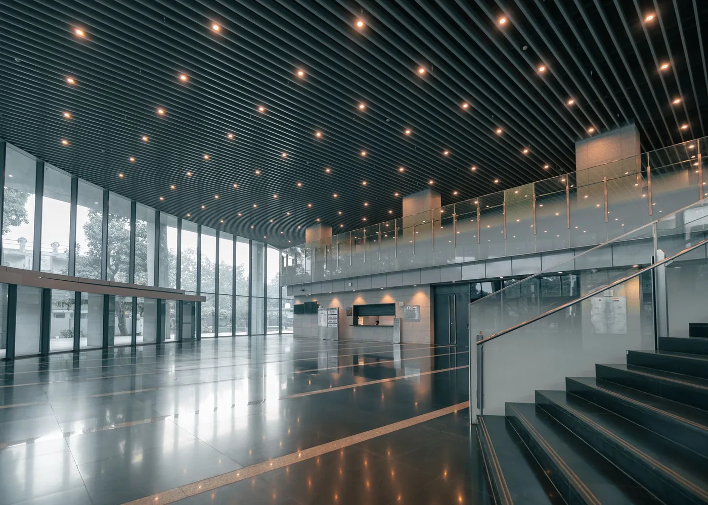 The foyer of a multi storey building with a mezzanine, an open staircase and full height glazing