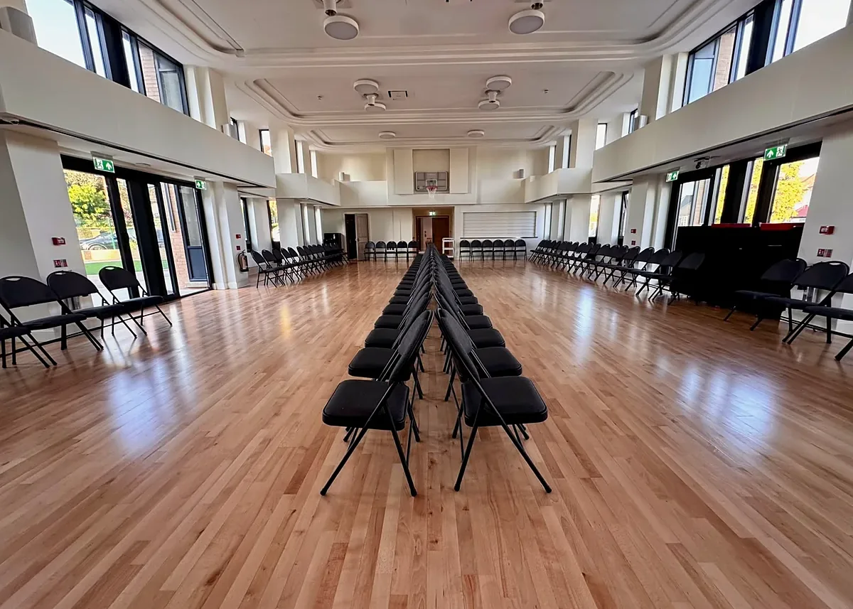 Father Michael Hall at The Ark in Golders Green, a double height hall with a coffered ceiling, galleries on both sides, full height windows and a polished timber floor set out with rows of chairs