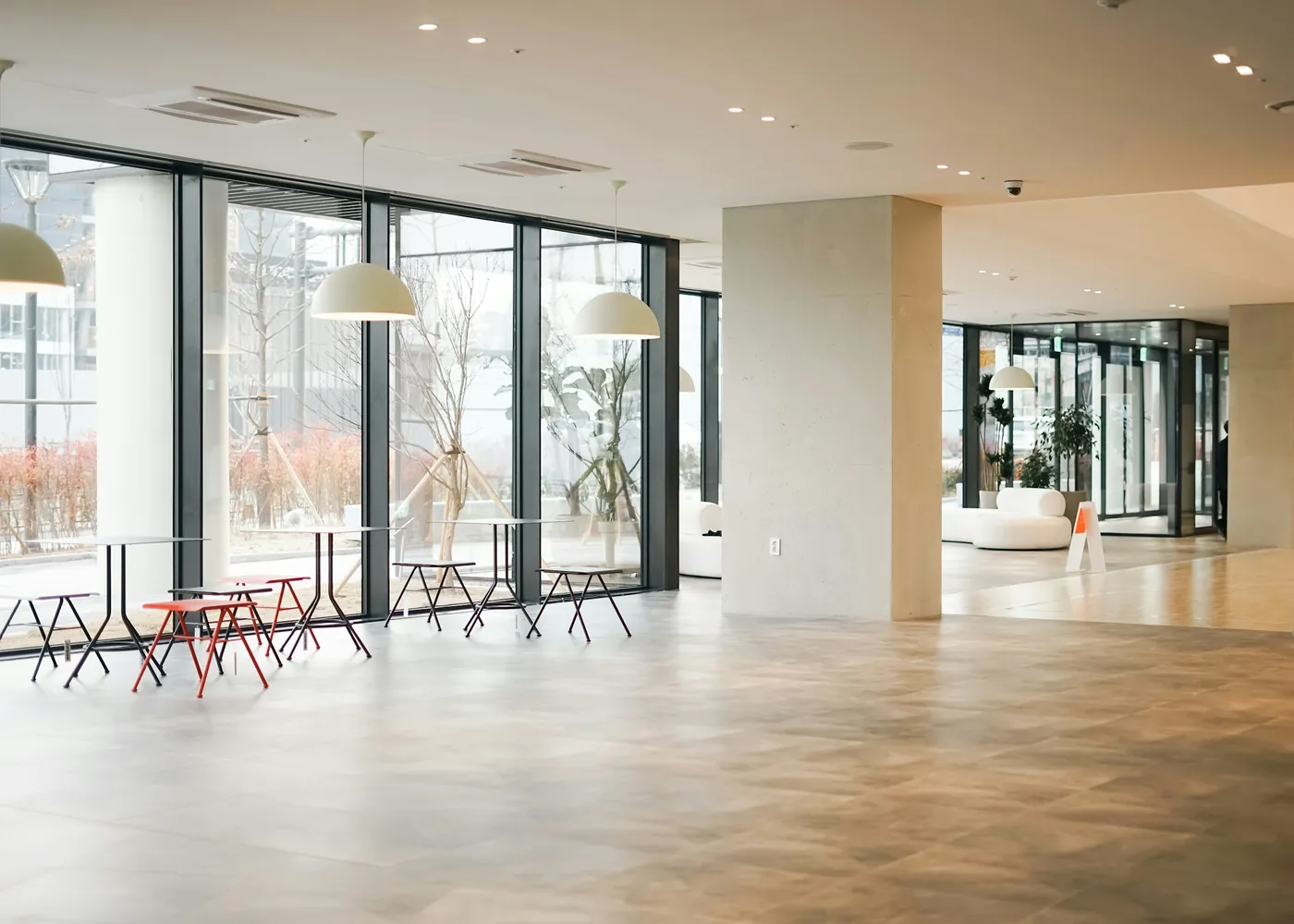 An empty ground floor commercial space with full height glazing, pale flooring and a few tables and chairs