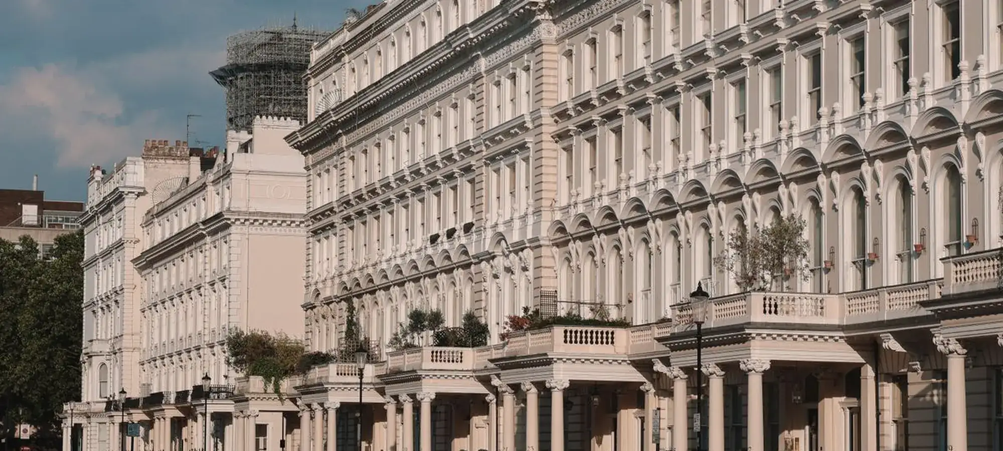 A long row of white stucco London townhouses lit by late afternoon sun